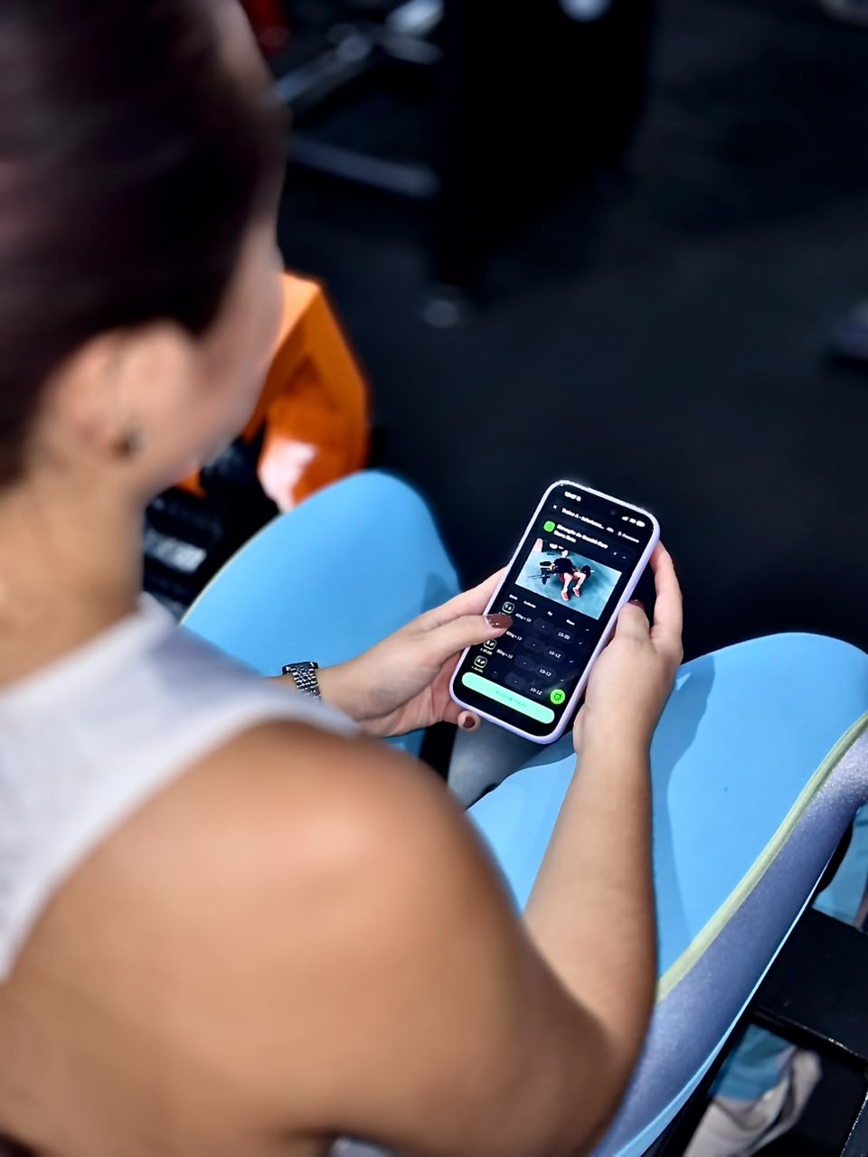Mulher sentada na academia consultando o treino no celular